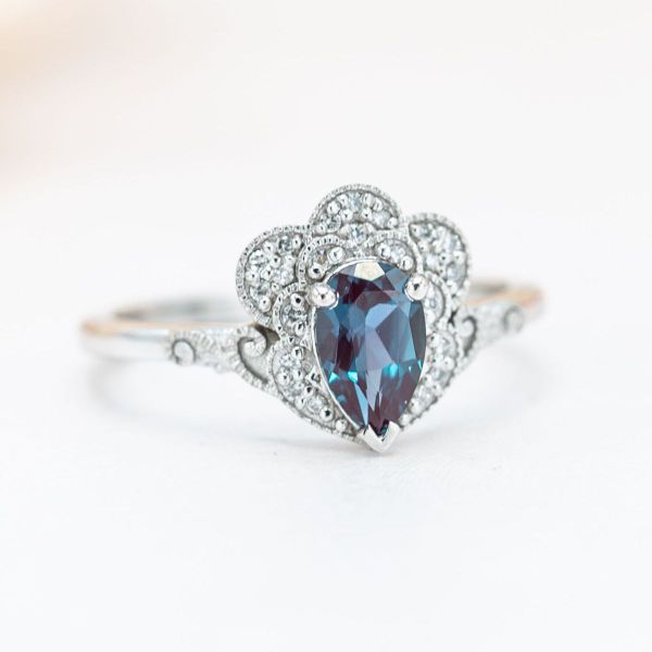 A scalloped halo surrounds the center stone alexandrite in this white gold engagement ring.