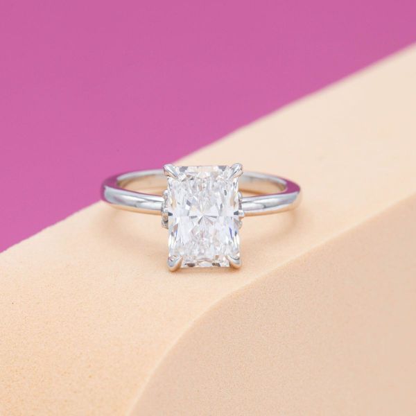 This engagement ring’s solitaire radiant cut diamond hides a scattering of diamonds in a hidden halo.
