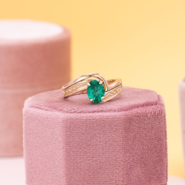 A faux tension setting of yellow gold holds this oval cut emerald.