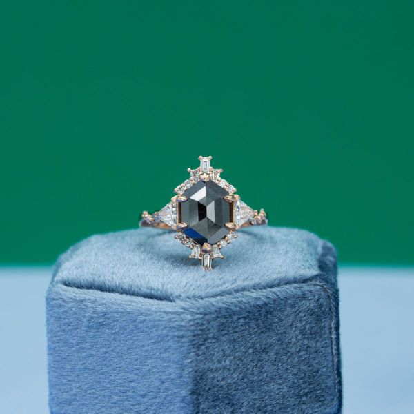 An almost black hexagon cut salt and pepper diamond sits in the center of this yellow gold engagement ring.