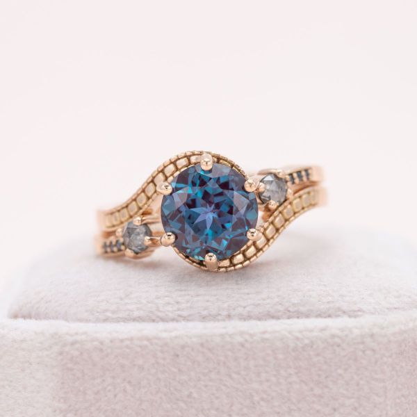 An alexandrite center stone is accented by salt and pepper diamonds in this yellow gold engagement ring.