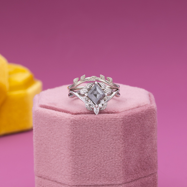 A stretched princess cut salt and pepper diamond is the center of a nature themed engagement ring.
