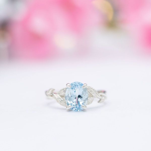 A baby blue oval cut aquamarine set in a bright white gold band of intertwining feathers.
