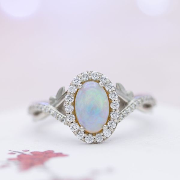 White opal engagement ring with a diamond halo and a twisting band with small leaf accents.