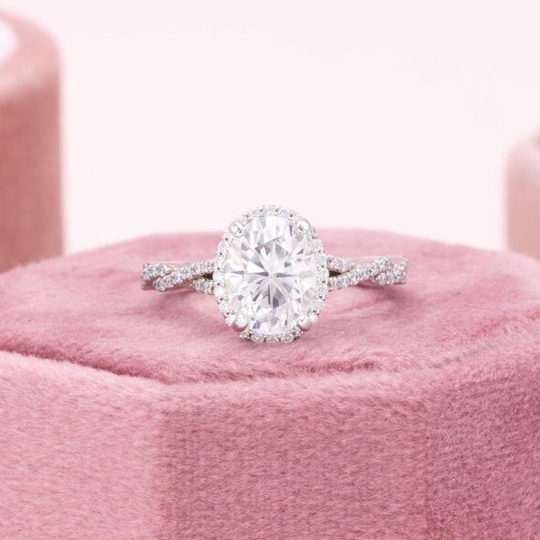Interlacing pavé-set moissanites twist up to an oval cut moissanite center stone surrounded by a shimmering moissanite halo in this dainty engagement ring.