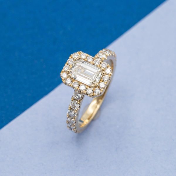 This vintage inspired engagement ring boasts yellow gold, an emerald cut lab diamond, and dozens of accent diamonds.
