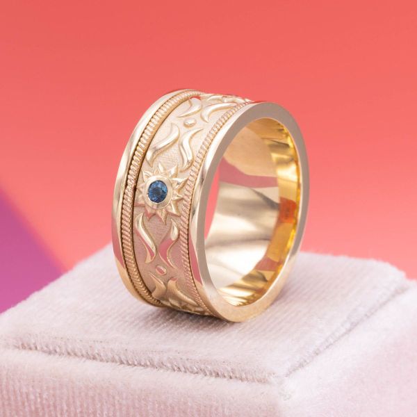 A diamond accented sunburst halo frames the salt and pepper diamond in Kate’s engagement ring while sun motifs bezel frame London blue topazes in Vincent’s matching band.