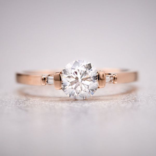 An open bar setting for the round center diamond and baguette cut side stones lets the gems sparkle, pairing them with a sleek, squared off rose gold band.