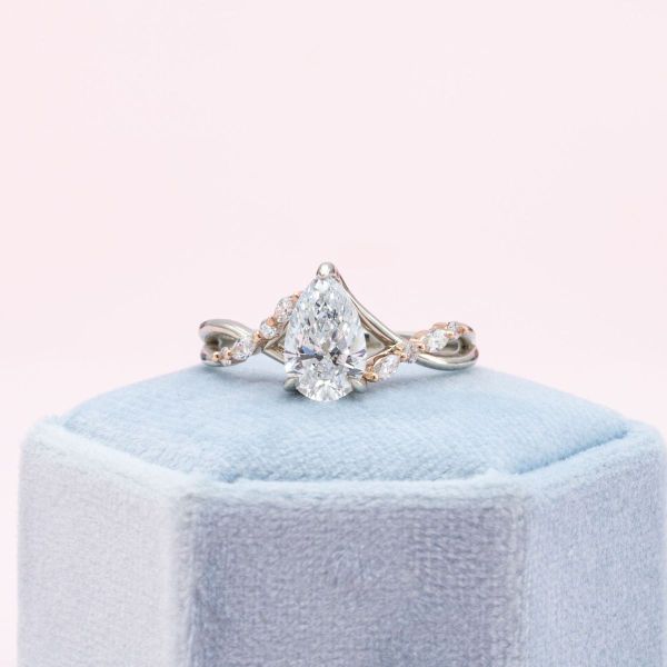 Sweeping lines in rose and white gold frame the pear cut diamond while marquise and round diamonds accent the band in this mixed metal engagement ring.