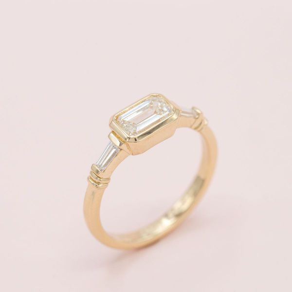 An east-west setting offers a unique take on this emerald cut diamond engagement ring.