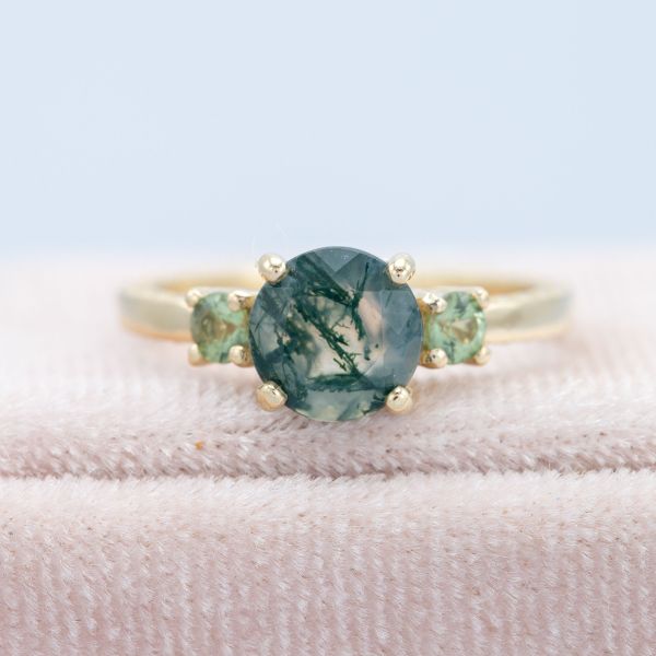 Three stone engagement ring with moss agate and green sapphire in a gold setting.