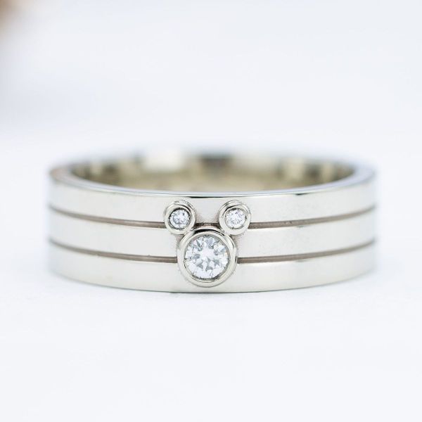 This polished white gold men’s engagement ring features bezel-set diamonds in a Mickey Mouse inspired design.