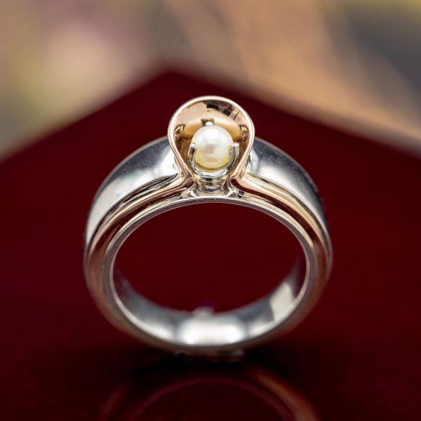 这个戒指设计创造了一个玫瑰金项圈作为一个美丽的设计元素，并围绕着珍珠中心石的一个保护盾。