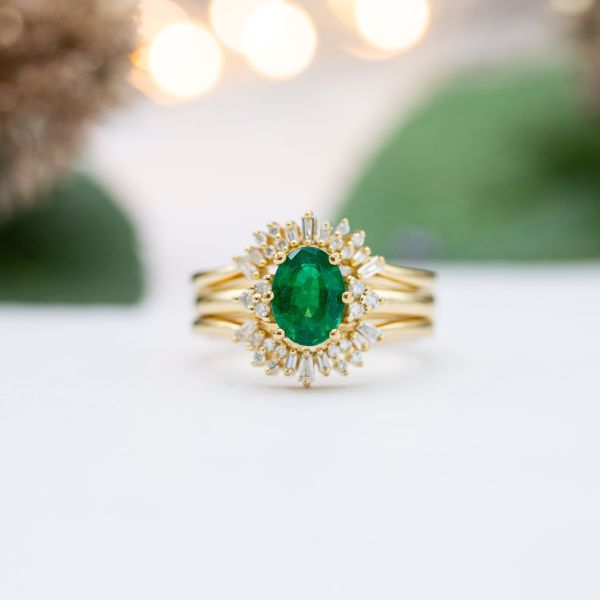 An oval emerald is the center of this yellow gold bridal set featuring a halo of marquise diamonds.