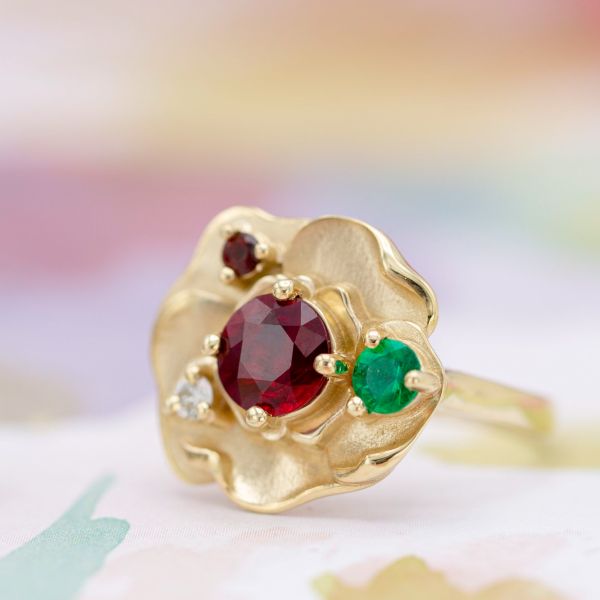 母亲的诞生石戒指用红宝石，祖母绿，钻石和石榴石在金玫瑰花瓣环境中。
