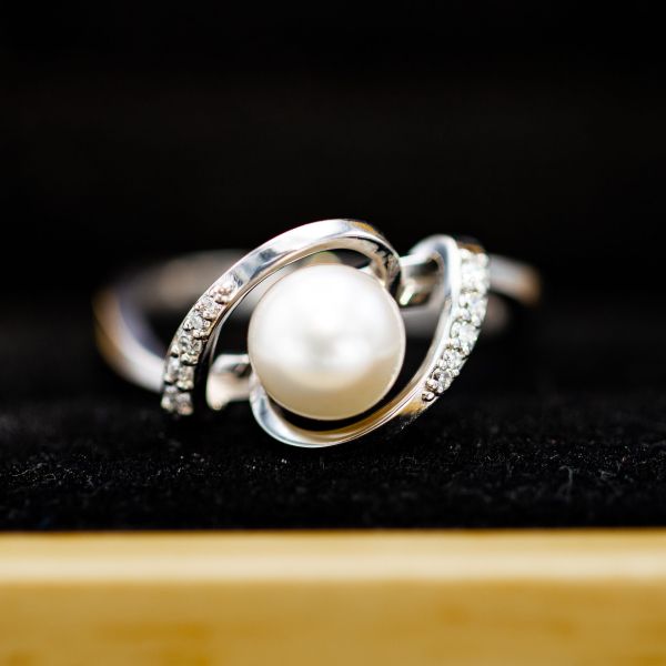 钻石镶嵌的曲线白金框架和保护珍珠中心石在这一雕塑订婚戒指。