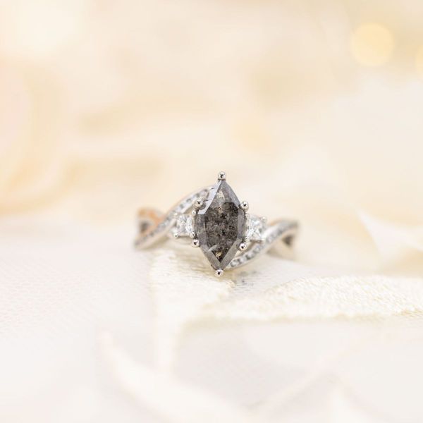 A marquise cut salt and pepper diamond is flanked by white diamond accents in a white gold setting.