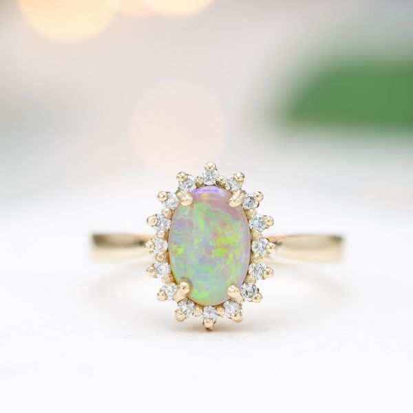 Crystal opal engagement ring with a diamond sunburst halo and tapered gold band.