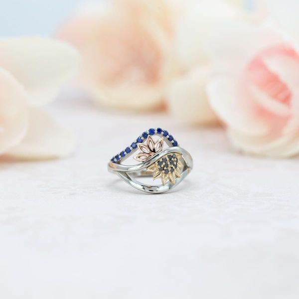 一枚大胆的混合金属订婚戒指，以蓝宝石和黑钻石为重点，点缀着向日葵和太阳花的细节。