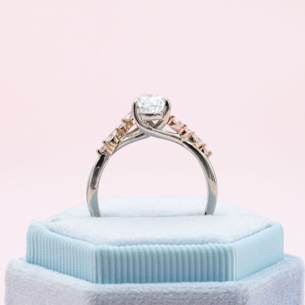 Sweeping lines in rose and white gold frame the pear cut diamond while marquise and round diamonds accent the band in this mixed metal engagement ring.