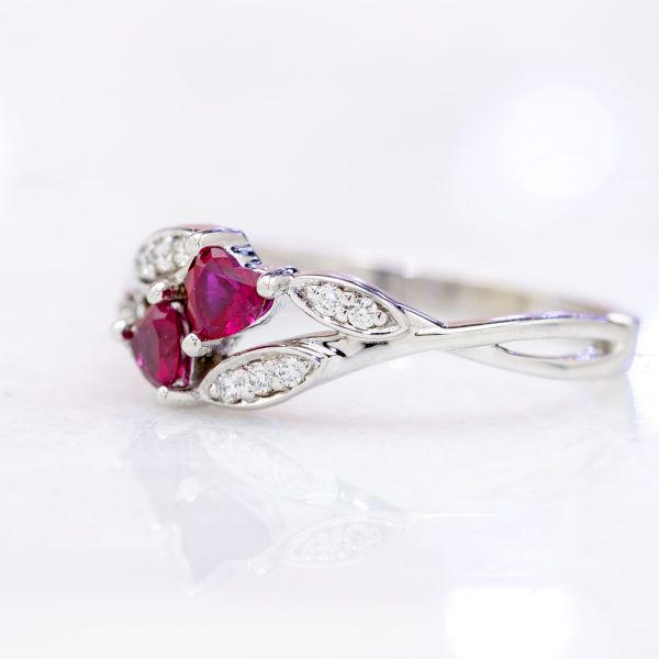 Delicate, vining diamond-studded leaves surround a setting of two heart cut rubies.