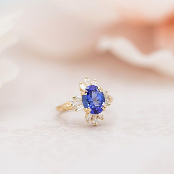 A unique take on a ballerina halo of tapered baguette diamonds surrounds an oval blue tanzanite center stone.