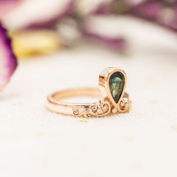Moissanite accents sit either side of a green sapphire on a rose gold band.