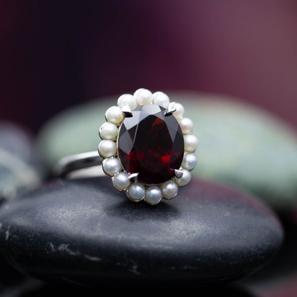 A stunning vintage-inspired scalloped halo of seed pearls contrasts the deep red garnet center stone.