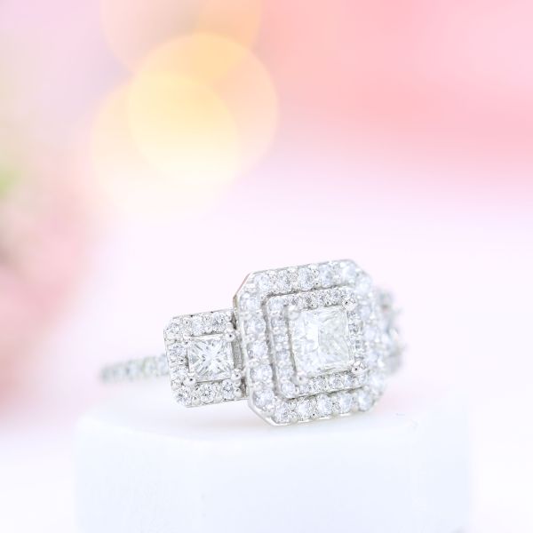约2500美元的重彩钻石在这枚迷人的三石戒指上形成了双光环和half-pavé戒指。因为有这么多钻石，选择实验室制造的重音钻石可以节省近900美元。