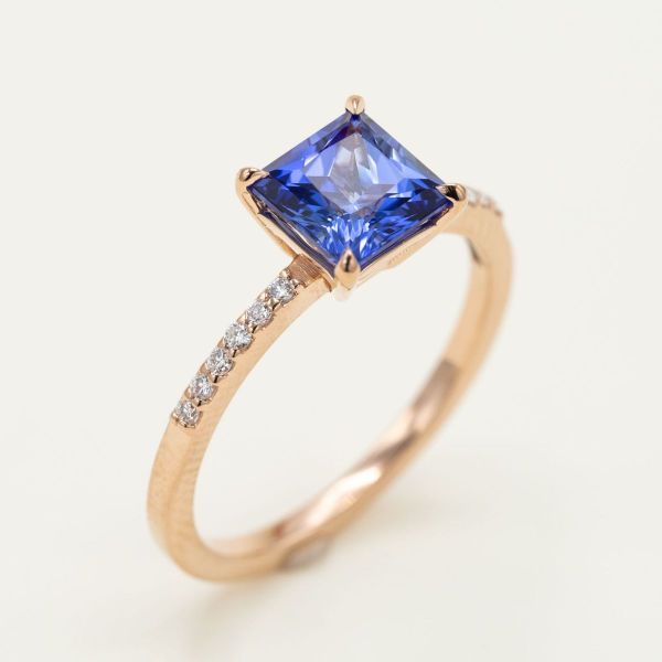 A yellow gold pave setting of diamonds makes this princess cut blue sapphire sparkle like the sea