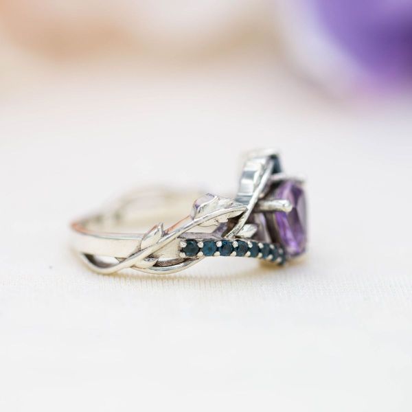 Watery blue topaz gemstones and a vining band center a trillion cut amethyst in this witchy engagement ring.