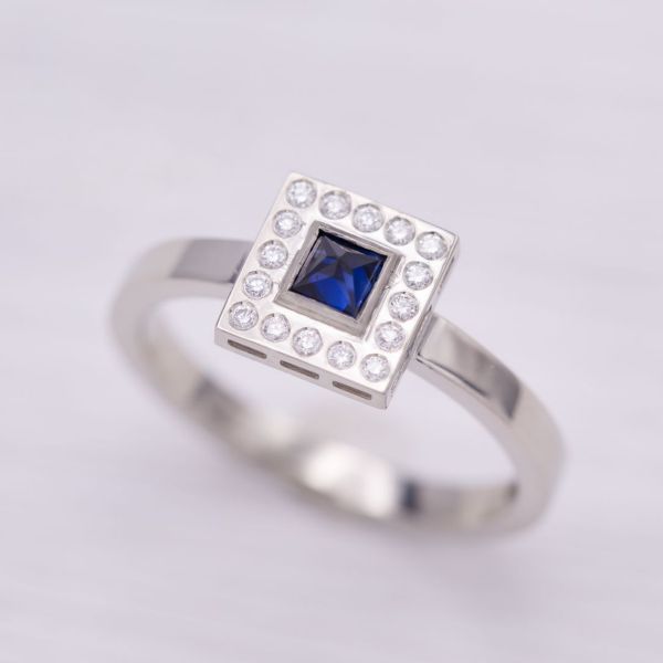 This ring is all angles, with a perfectly square halo of flush set diamonds surrounding a bezel set princess cut sapphire.