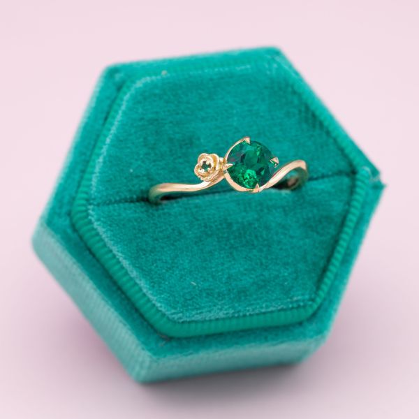 A delicate yellow gold band swirls around a brilliant cut emerald.