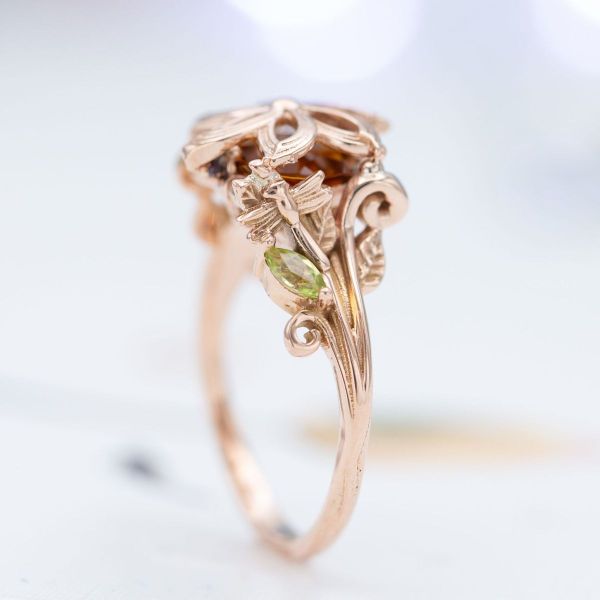 A little dragonfly sits on the rose gold leaves of this citrine center stone engagement ring.