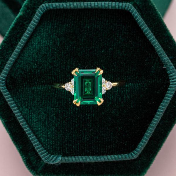 Double claw prongs hold the emerald at the center of this engagement ring with diamond side stones.