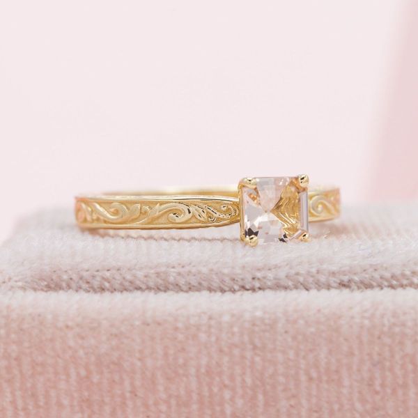 The X shape at the center of the Asscher cut morganite is reflected in the tapered yellow gold band of this engagement ring.