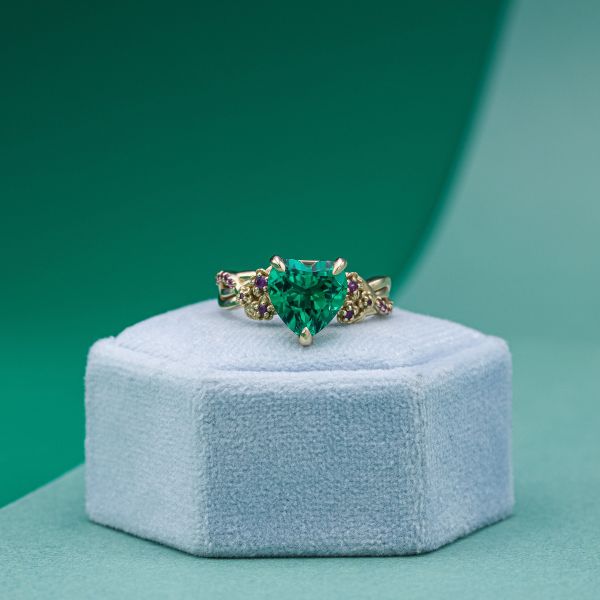 A heart shaped emerald sits in yellow gold with dots of colored stones throughout.