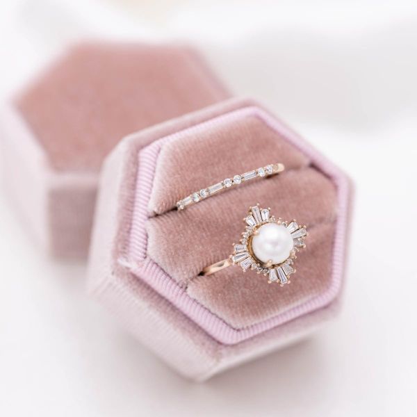 A pearl engagement ring with a baguette diamond halo and matching diamond-lined wedding band.