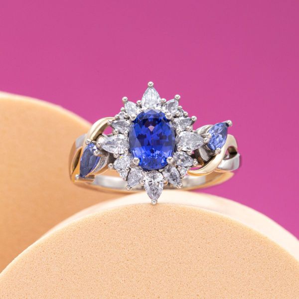 For this engagement ring we frame a light blue oval sapphire with a shimmering diamond halo. But don’t stop there! We injected a little modern magic into this classic design by adding a two-tone white and yellow gold twisted band and found space for two more sapphire accents!