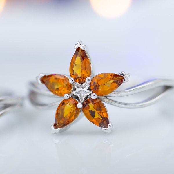 这枚空灵的订婚戒指的花瓣由五片梨形橘晶组成。