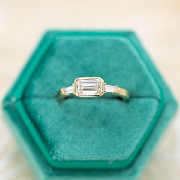 An east-west setting offers a unique take on this emerald cut diamond engagement ring.