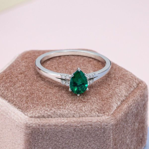 A split shank band and cathedral setting add drama to this pear cut emerald engagement ring.