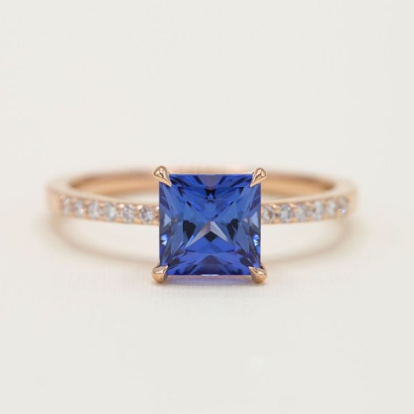A yellow gold pave setting of diamonds makes this princess cut blue sapphire sparkle like the sea