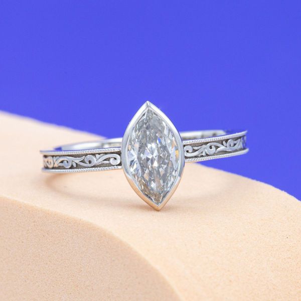 A marquise cut diamond is paired with an intricately engraved band in this engagement ring.