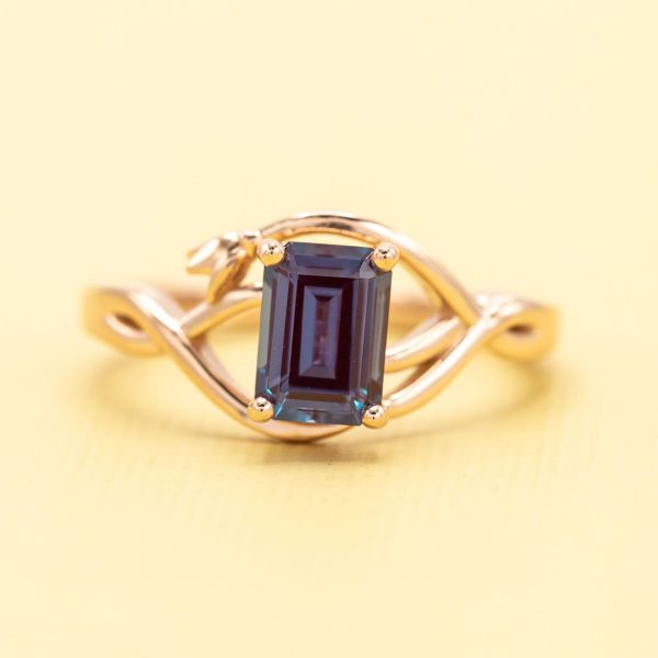 An emerald cut alexandrite cits in the center of this rose gold engagement ring.