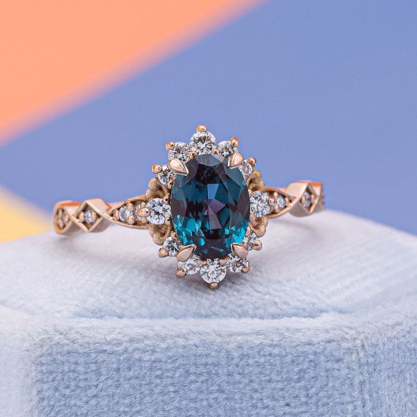 An oval cut alexandrite sits in a rose gold band with diamond accents giving an antique engagement ring vibe.
