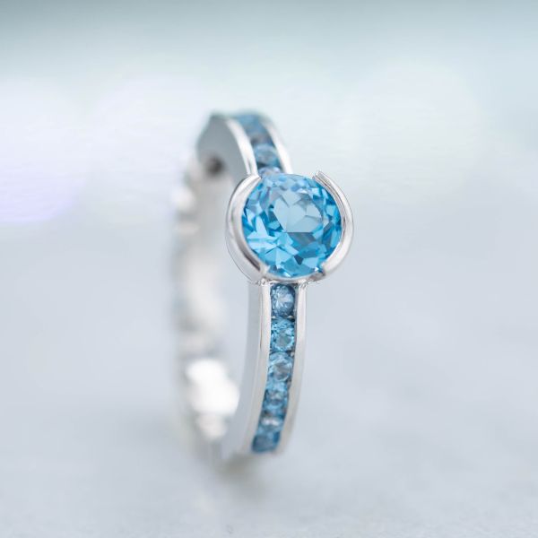 A modern semi-bezel setting for this round Swiss blue topaz is flanked by channel set pave of the same gem.