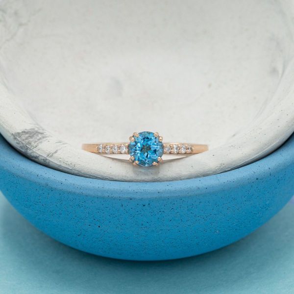 Rose gold double-prongs hold a sky blue topaz as diamond accents dance along this engagement ring’s shoulders.