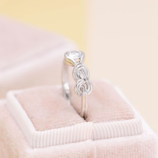 A ring designed for climbing enthusiasts, this setting has a moissanite at the center of a white gold band with a figure 8 knot to the right of the stone.