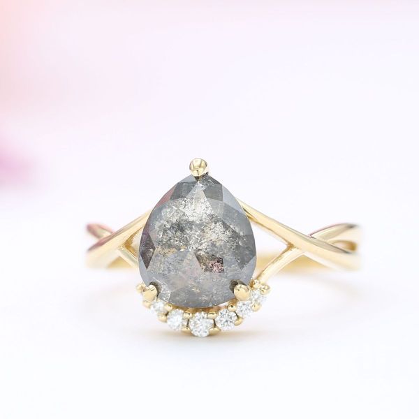 A chubby pear cut salt and pepper diamond is held in a yellow gold split shank setting.